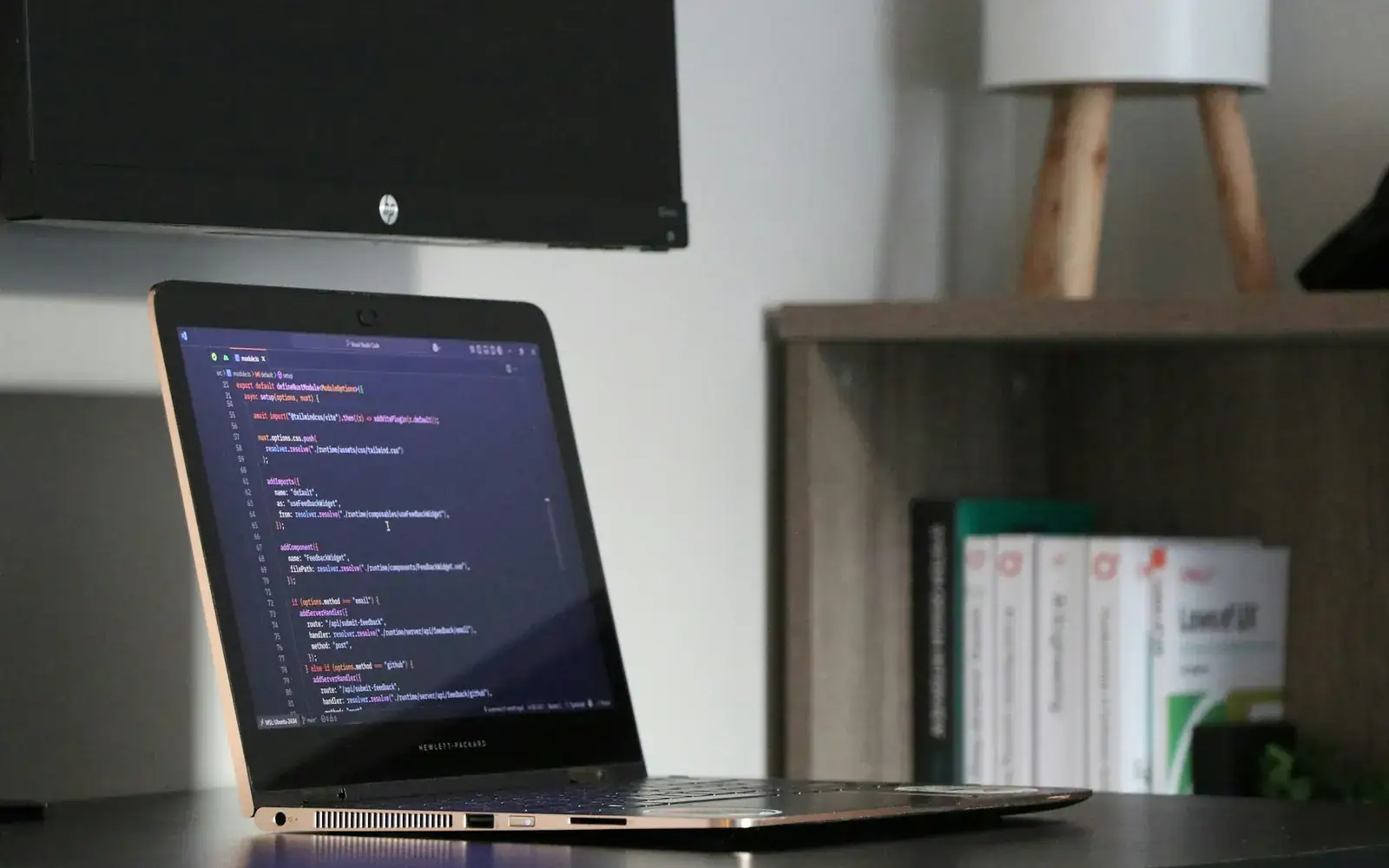 Laptop dengan kode aplikasi di meja kerja dekat rak buku